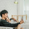 Happy Asian Lover sitting and using the digital smart mobile phone to selfie over the sofa of living room at modern home, Couple successfull and lifestyle concept